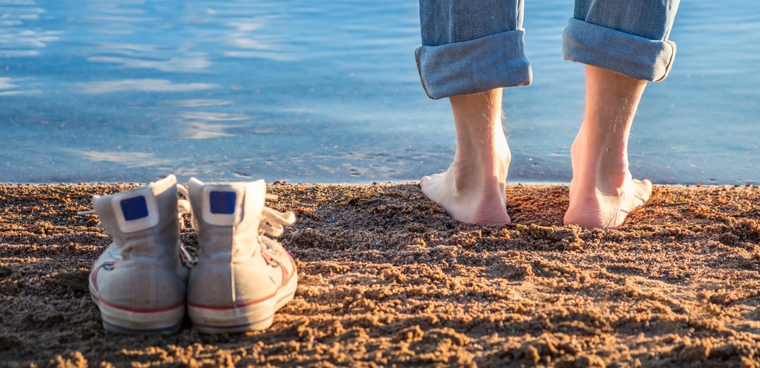 Person står barfodet på stranden.